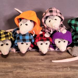 stack of stuffed plushie opossums each wearing a different colored hoodie that says "Anything is Possum-ble"